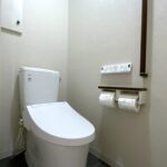 グレージュの壁紙を背景に、スタイリッシュな黒の手すりとLIXIL便器が綺麗に収まった、マンションのトイレリフォーム完成写真。