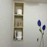 リフォーム前のトイレの壁面埋込収納。扉がなくトイレットペーパーや掃除用品が丸見えになって生活感が出ている状態。