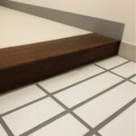 リフォーム前の木製上がり框と玄関タイルの足元写真。