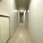 ペールグレーのフローリング床と壁と同色に塗装された建具がすっきり続くリフォーム後の廊下。
