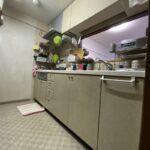 ベージュ系の開き扉パネルと従来の床材で構成された施工前のマンションキッチン